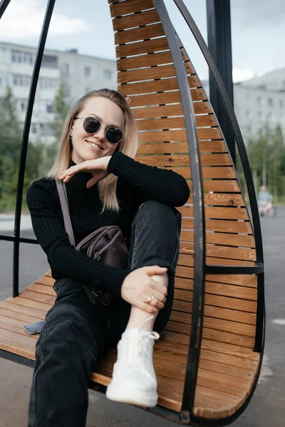 Genç güzel beyaz kız parkta bir hamak sandalyesinde oturuyor. Havalı hippi kadın kameraya bakar ve gülümser.