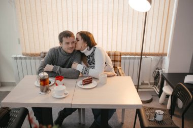 Sevimli bir çift, bir kafede tatlı yiyip sarılıyorlar.