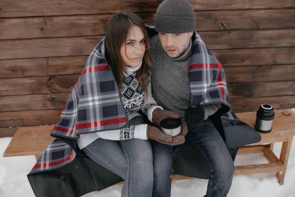 Giovane coppia innamorata nel bosco crogiolarsi sotto una coperta. Bevono il tè da un thermos — Foto Stock