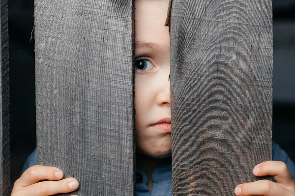 Close-up van een jonge mannelijke man die uitkijkt van achter een rustieke houten hek, kijkend in de camera — Stockfoto