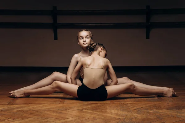 Изображение двух красивых молодых балерин, делающих сплит, растягивающих ноги в позе на сцене, в студии. Элегантный исполнитель, гибкость концепции, прочность дисциплины, физическая работа. — стоковое фото