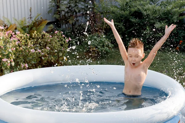 Ein fröhliches fünfjähriges Kind spielt im Pool. lustige Junge planscht in einem aufblasbaren Pool mit einem sonnigen fliegenden Tag. — Stockfoto