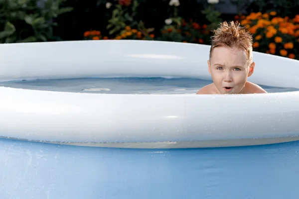 Netter kleiner Junge schwimmt im Pool und hat Spaß. Lustiges fünfjähriges Kind schwimmt an einem sonnigen Sommertag in einem aufblasbaren Pool an der Datscha — Stockfoto