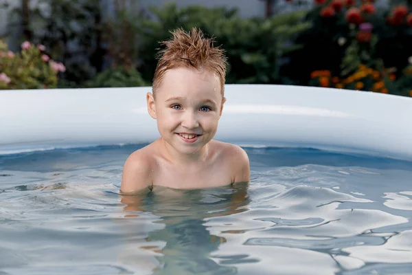 在阳光灿烂的日子里，一个微笑的五岁男孩在外面的一个蓝色游泳池里玩乐的特写 — 图库照片