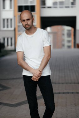 Beyaz tişörtlü, gri arka planda yakışıklı, kel bir adamın resmi.. 