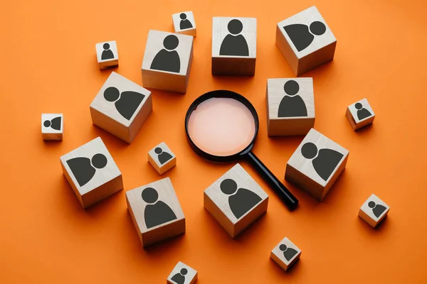 Wooden cubes with the image of a man lie next to a magnifying glass on an orange background. The concept of talent search or employee concept search using a magnifying glass