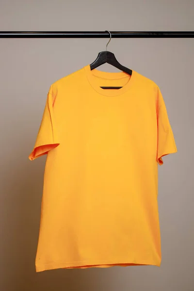 Tomma gula T-shirt hängande på en hängare på en grå bakgrund. Mock up för design Stockfoto