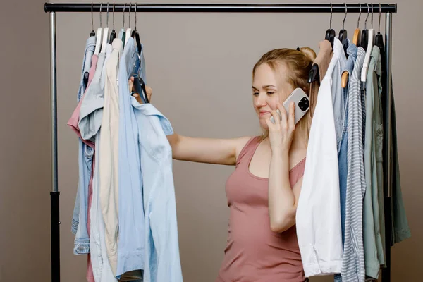 Charmig ung dam talar på en mobiltelefon bland fashionabla kläder i provrummet i butiken, berätta för sin vän om försäljningen. Begreppet stil, mode, shopping och konsumtion. Stockbild