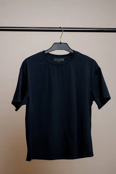 En tom svart T-shirt väger på en galge på en neutral bakgrund. Mock up för design. Stockfoto