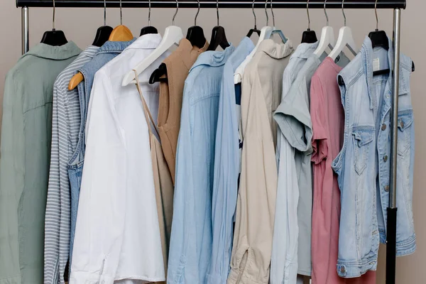 Närbild av en färgstark variation av skjortor, T-shirts och blusar på hängare inne i garderoben. butik av pastellfärgade kläder. Ekologiska bomullskläder. Selektiv inriktning. Stockbild