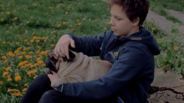 Üzgün Ukraynalı mülteci çocuk karahindiba dolu bahçede oturmuş köpeğini okşuyor. Kucağında yatan köpek.