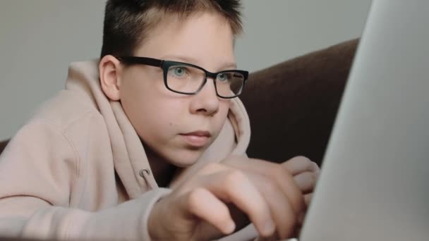 Teenage Caucasian Boy Hoodie Wearing Eyeglasses Using Laptop Laying Couch — Vídeo de stock