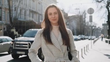 Güneşli bir günde sokakta gri ceketli gülümseyen genç bir kadının portresi. El bilgisayarı ağır çekim orta çekim.