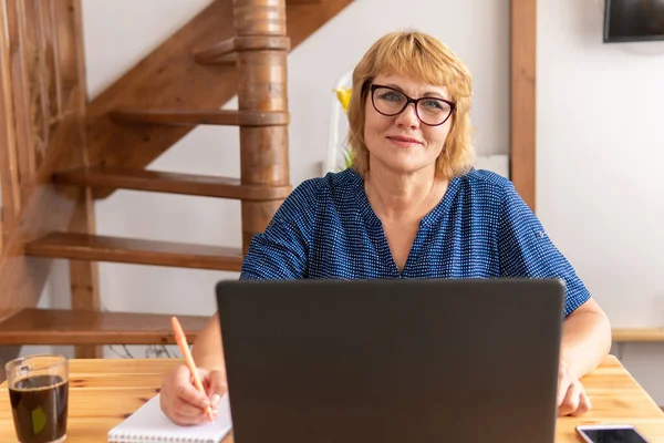 Una mujer está sentada en una habitación en una mesa con un portátil. — Foto de Stock