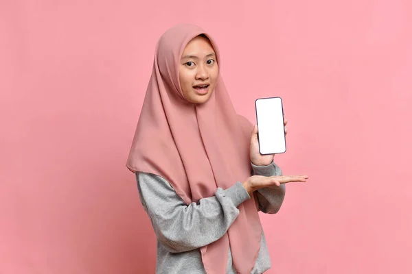 ショックを受けた美しいアジア系ムスリム女性の肖像画ピンクを背景に電話で白い画面を示す — ストック写真