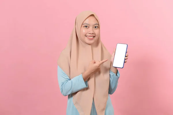 一个快乐的亚裔穆斯林女商人在粉色背景下展示空白屏幕手机的肖像 — 图库照片