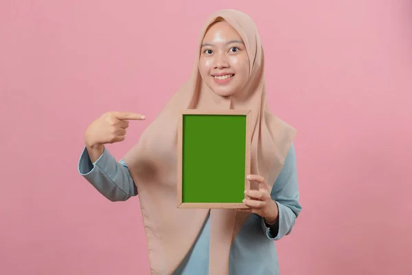 美しい若いイスラム教徒の女性は ピンクの背景に黒板に何かを指して示します — ストック写真