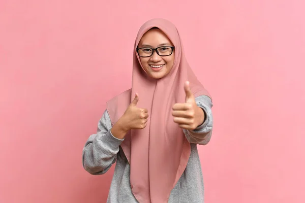 Genç Asyalı Müslüman kadın pembe arka planda baş parmak gösteriyor. Kopyalama alanı oluşturun. Baş parmaklar gösteriliyor.