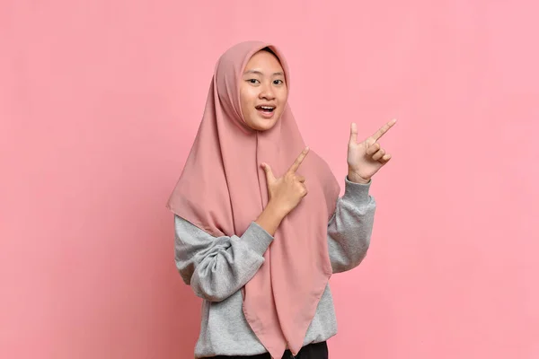 亚洲美丽的年轻穆斯林女子的画像 她用手指指向双手上方 与粉红背景隔离 — 图库照片