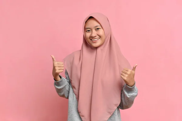Genç Asyalı Müslüman kadın pembe arka planda baş parmak gösteriyor. Kopyalama alanı oluşturun. Baş parmaklar gösteriliyor.