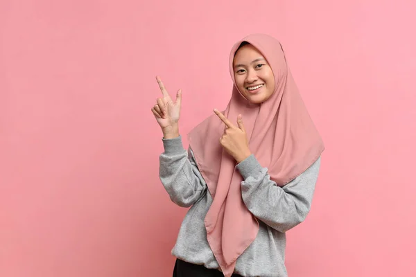 アジアの美しい若いイスラム教徒の女性の肖像画は ピンクの背景に隔離された笑顔の顔の上側に指で両手を指す — ストック写真