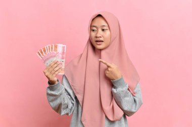Endonezya parası taşıyan Endonezyalı genç bir kadın pembe arka planda izole edilmiş paralar tutuyor.