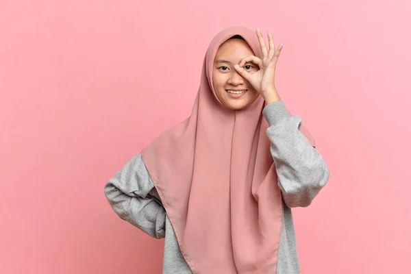 若いイスラム教徒の女性は良いジェスチャーを示し 指を通してカメラを見て ピンクの背景に隔離された — ストック写真