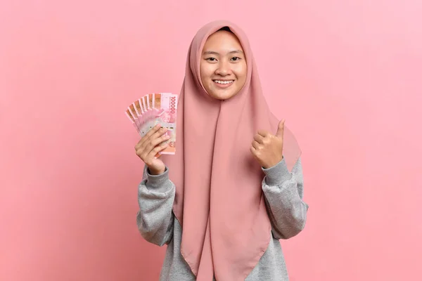 Uśmiechnięta Muzułmanka Hidżabie Trzymająca Banknoty Idr Odizolowana Różowym Tle Obraz Stockowy