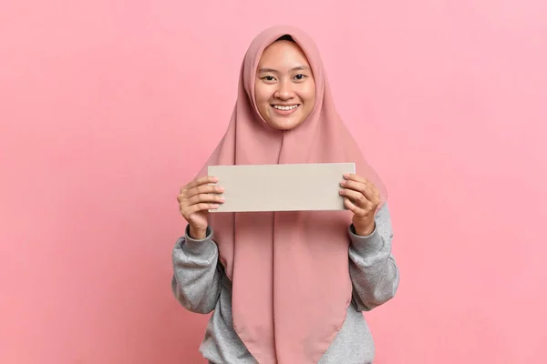 Happy smiling Muslim woman holding white board isolated on pink background