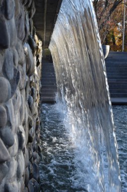 Parkta akan bir şelale. Bahçedeki bir çeşmenin şelalesi. Su duvarı. Şelalenin güzel manzarası. Yapay şelale, şehir çeşmesi, yakın çekim suyu.