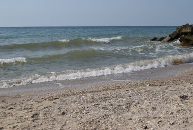 Vahşi bir sahilde kaya parçaları. Gökyüzü berraktı ve denizin suları kayalara vuruyordu.