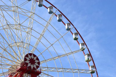 Şehir parkında mavi gökyüzüne karşı dönmedolap ve fotokopi alanı. Dönme dolabın beyaz metal yapısının bir parçası. Mavi gökyüzüne karşı beyaz bulutlu gözlem taksileri var.