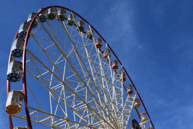 Şehir parkında mavi gökyüzüne karşı dönmedolap ve fotokopi alanı. Dönme dolabın beyaz metal yapısının bir parçası. Mavi gökyüzüne karşı beyaz bulutlu gözlem taksileri var.