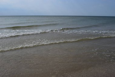 Güzel manzara - turkuaz renkli deniz suyu, kum, gökyüzü. Dalgalar kıyıya vuruyor. Plaj ve Su Sıçratan Dalgalar