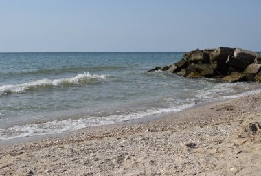 Vahşi bir sahilde kaya parçaları. Gökyüzü berraktı ve denizin suları kayalara vuruyordu.