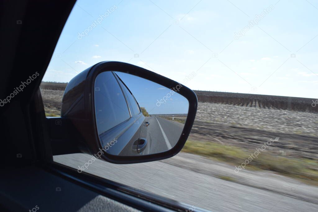 Reflected road in rearview mirror. View from car side mirror driving on asphalt road. Summer day. Auto tourism, traveling by car concept. Shooting from the passenger seat. travel along the road field