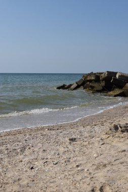 Vahşi bir sahilde kaya parçaları. Gökyüzü berraktı ve denizin suları kayalara vuruyordu.