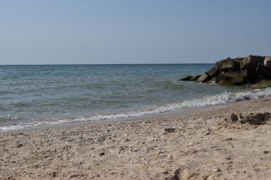 Vahşi bir sahilde kaya parçaları. Gökyüzü berraktı ve denizin suları kayalara vuruyordu.
