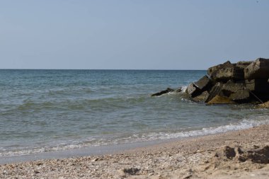 Vahşi bir sahilde kaya parçaları. Gökyüzü berraktı ve denizin suları kayalara vuruyordu.