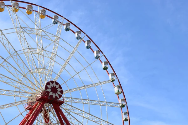 Şehir parkında mavi gökyüzüne karşı dönmedolap ve fotokopi alanı. Dönme dolabın beyaz metal yapısının bir parçası. Mavi gökyüzüne karşı beyaz bulutlu gözlem taksileri var.