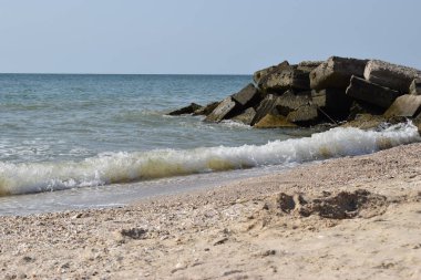 Vahşi bir sahilde kaya parçaları. Gökyüzü berraktı ve denizin suları kayalara vuruyordu.