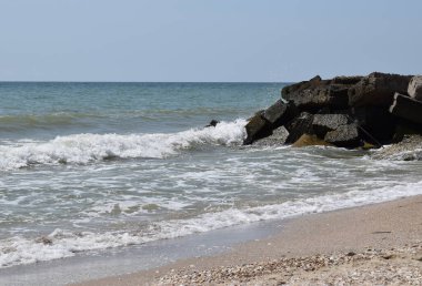 Deniz dalgaları. Açık havada yüksek dalgalar. Denizde güneşli bir gün. Arka plan mavi deniz dalgaları. Islak taşlar ve dalgalar. Tasarım için deniz taşlarının ve deniz kölesinin arka planı.