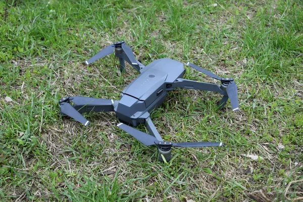 Mini drone unfolded on a grass before take-off. Small drone flies in sky over the park taking video and photos. Remote control air delivery and spy.
