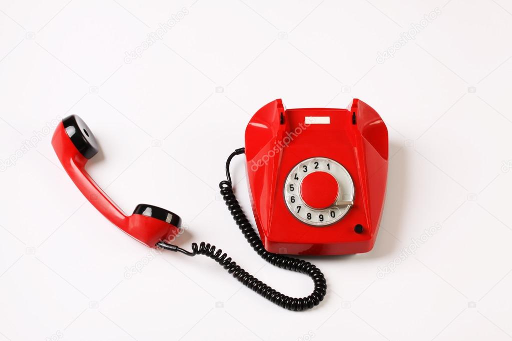 Red rotary telephone off hook on white background