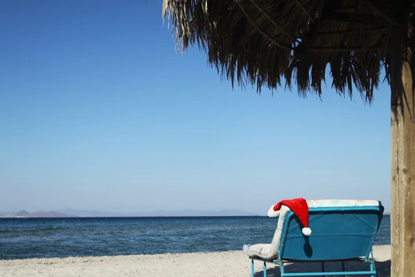 Santa claus klobouk na pláži pod slunečníkem — Stock fotografie