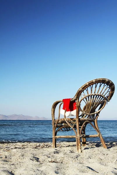 Sombrero de Santa Claus en barandilla de soporte de silla de ratán en la playa —  Fotos de Stock