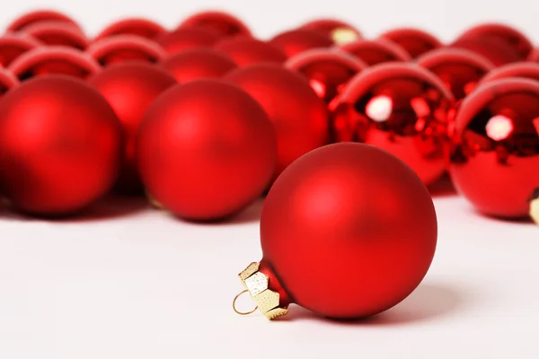 Rote matte Weihnachtskugel vor einer Gruppe von matten und glänzenden Weihnachtskugeln auf weißem Hintergrund — Stockfoto