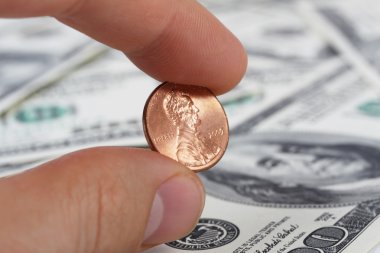 Detailed view of male hand holding a penny on background with money american hundred dollar bills clipart