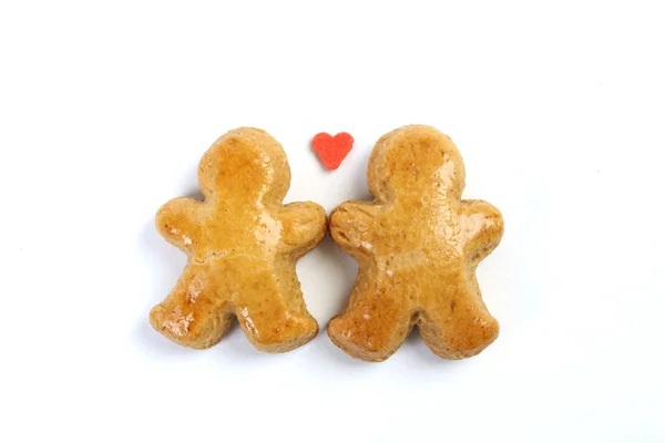 Dos pequeños enamorados figura de pan de jengibre sobre fondo blanco y en medio de dos pequeña figura es un corazón rojo dulce . —  Fotos de Stock