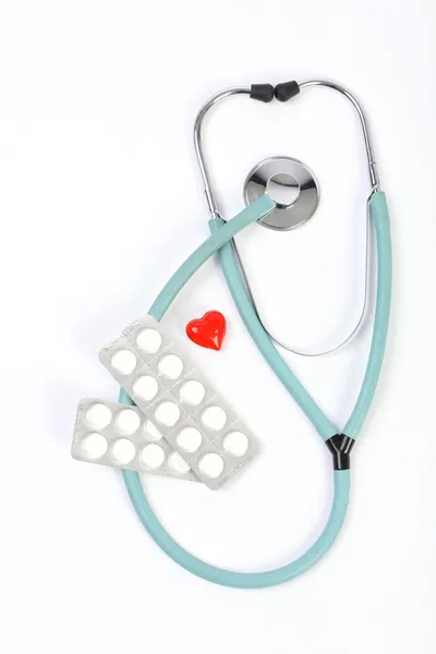 Medici stetoscopio blu, pillole e un piccolo cuore rosso su sfondo bianco — Foto Stock